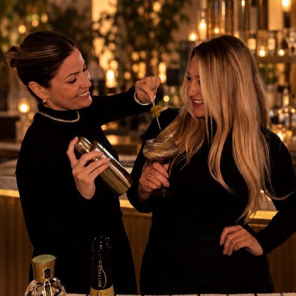 Two Cocktail Edit bartenders in black, sharing a laugh behind a hotel bar