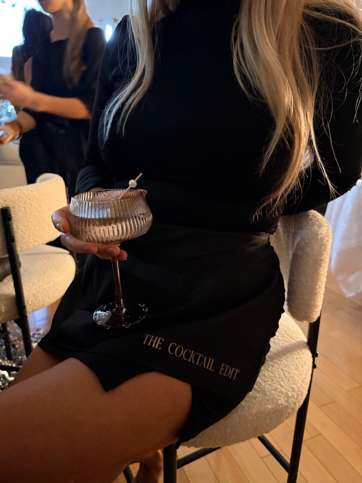 A guest holding a coupe, wearing a The Cocktail Edit apron